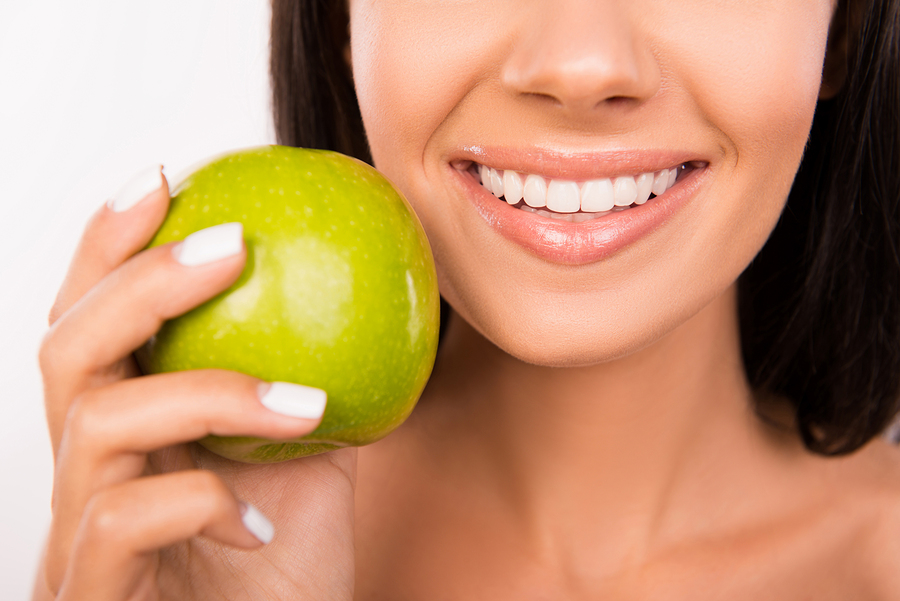 woman smiling nice teeth, holding green apple. Jersey City, NJ dental implants