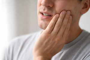 Person holding jaw in pain, focus on lower face showing dental discomfort