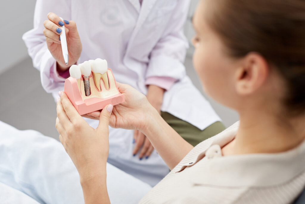 Dentist pointing at tooth model while consulting patient about dental implants